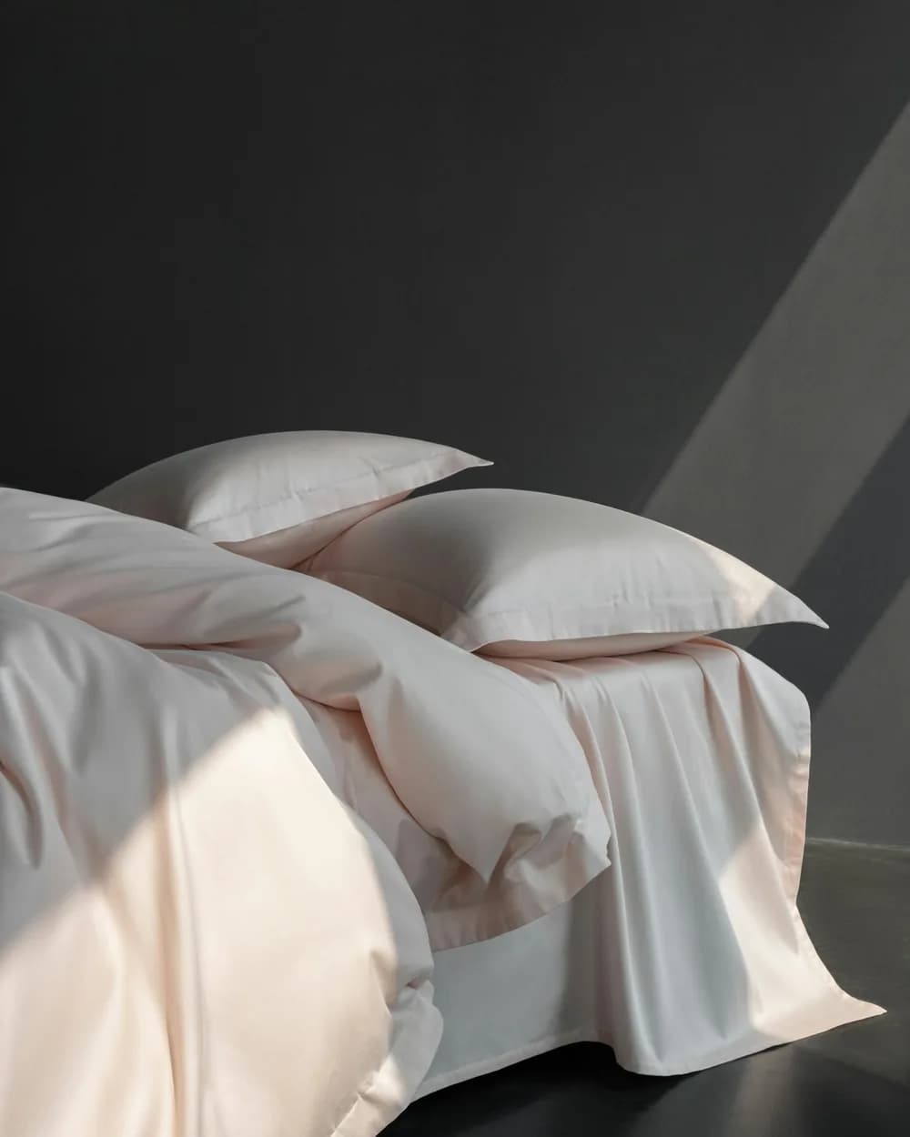 A bed made with blush cotton sheets and pillows